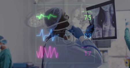 Photo for Image of vital signs readings over african american male surgeon studying x ray. Medical and healthcare services concept digitally generated image. - Royalty Free Image