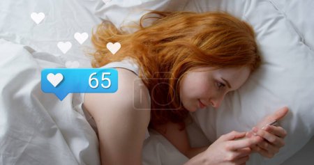 Image of social media reactions over caucasian woman using smartphone in bed. Social media, network, communication and technology concept digitally generated image.