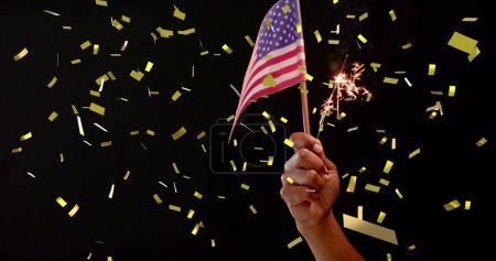 Téléchargez les photos : Image de confettis tombant sur la main tenant le drapeau des États-Unis d'Amérique et scintillant. Indépendance américaine, tradition et concept de célébration image générée numériquement. - en image libre de droit