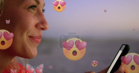Photo for Image of emoticons over profile of happy biracial woman using smartphone at beach. global connections, social media, technology and digital interface concept digitally generated image. - Royalty Free Image