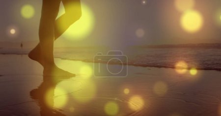 Photo for Glowing yellow spots of light against mid section of a woman walking on the beach. Love and relationship concept - Royalty Free Image