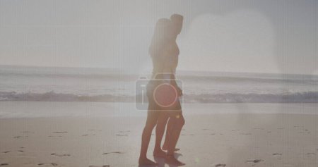 Image of light spots over caucasian couple walking at beach. Holidays and digital interface concept digitally generated image.
