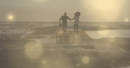 Foto de Puntos brillantes de luz contra una pareja afroamericana cogida de la mano corriendo sobre las rocas. Concepto de amor y relación - Imagen libre de derechos