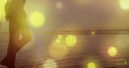 Foto de Manchas amarillas brillantes de luz contra la sección media de una mujer caminando por la playa. Concepto de amor y relación - Imagen libre de derechos
