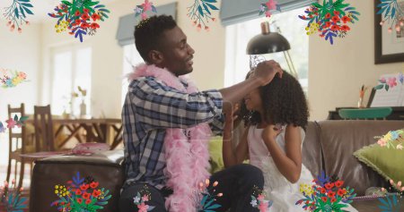 Image of flowers over happy african american father putting crown to daughter at home. family life, childhood, love and care concept digitally generated image.