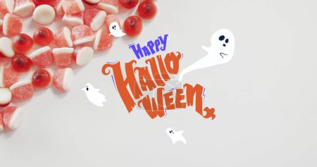 Fröhliches Halloween-Textbanner und Geistersymbole gegen Großaufnahme von Zuckerhühnern auf weißer Oberfläche. Halloween-Fest und Festkonzept