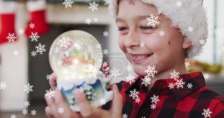 Photo for Image of snow falling at chrsitmas over happy caucasian boy with snow globe. christmas and celebration concept digitally generated image. - Royalty Free Image
