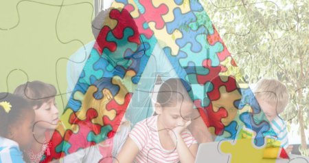 Bild von Puzzleteilen über verschiedene Schüler und Lehrer mit Laptop. Monat des Autismus-Bewusstseins und Feier-Konzept digital generiertes Bild.