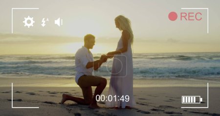 Photo for Image of a young Caucasian man proposing to a young Caucasian woman, seen on a screen of a digital camera in record mode with icons and timer - Royalty Free Image