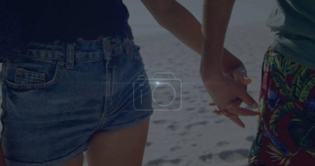 Téléchargez les photos : Point de lumière contre la partie médiane d'un couple afro-américain tenant la main sur la plage. Concept d'amour et de relation - en image libre de droit
