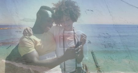 Foto de Imagen de una feliz pareja afroamericana usando un smartphone en la playa sobre el mar. naturaleza, vacaciones e imagen generada digitalmente en verano. - Imagen libre de derechos