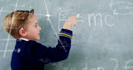 Foto de Imagen de fórmulas matemáticas sobre niño caucásico escribiendo en pizarra. aprendizaje, educación y concepto escolar imagen generada digitalmente. - Imagen libre de derechos