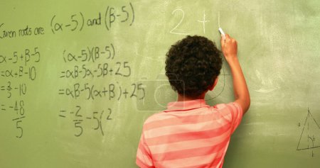 Foto de Imagen de fórmulas matemáticas sobre la vista posterior de un niño birracial escribiendo en una pizarra negra. aprendizaje, educación y concepto escolar imagen generada digitalmente. - Imagen libre de derechos