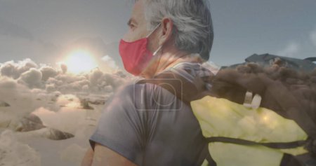 Téléchargez les photos : Homme âgé caucasien en masque facial marchant sur la côte, sur des nuages en mouvement rapide. retraite active et saine et liberté pendant le concept de pandémie de coronavirus,, image générée numériquement. - en image libre de droit