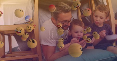 Foto de Imagen de la caída de emoji sobre la familia caucásica feliz pasar tiempo juntos. concepto del día de los niños, imagen generada digitalmente. - Imagen libre de derechos