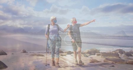 Téléchargez les photos : Couple âgé caucasien masques visage randonnée sur la côte, au-dessus de la mer en mouvement. retraite active et saine et liberté pendant le concept de pandémie de coronavirus,, image générée numériquement. - en image libre de droit