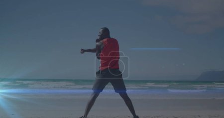 Foto de Imagen de un punto de luz azul contra la vista trasera del hombre afroamericano en forma estirándose en la playa. Concepto de tecnología deportiva y fitness, - Imagen libre de derechos