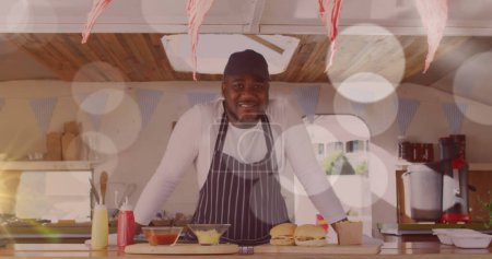 Photo for Image of spots of light floating over smiling african american fast food seller. small independent business concept, digitally generated image. - Royalty Free Image