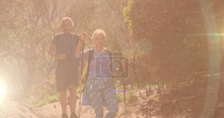 Kaukasisches Seniorenpaar beim Wandern auf dem Land, bei Linsenblitzen und Bokeh-Stadtlichtern. aktives, gesundes Outdoor-Rentenkonzept, digital generiertes Image.