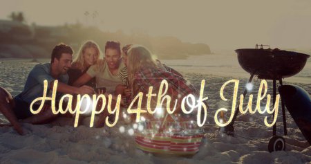 Foto de Imagen digital de oro Feliz 4 de julio saludo mientras el fondo muestra a diversos amigos riendo de algo en el teléfono móvil mientras beben y se sientan en la playa. 4k - Imagen libre de derechos