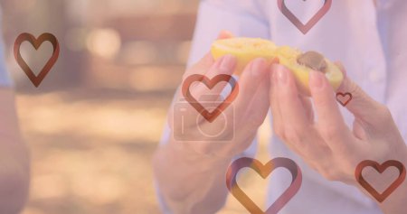 Photo for Image of hearts falling over caucasian woman eating fruits in park. fashion and lifestyle concept, digitally generated image. - Royalty Free Image