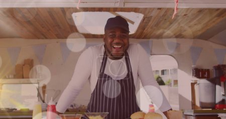 Téléchargez les photos : Image de spots de lumière flottant sur un vendeur de fast-food afro-américain souriant. concept de petite entreprise indépendante, image générée numériquement. - en image libre de droit