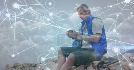 Photo for Caucasian senior man sitting on hillside taking photo with smartphone, over network of connections. active lifestyle, healthy retirement and global communication concept,, digitally generated image. - Royalty Free Image