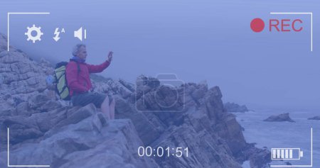 Photo for Smartphone image interface screen over caucasian senior man sitting on coast filming sea view. active retirement, communication and social media concept,, digitally generated image. - Royalty Free Image