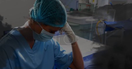 Photo for Image of black clouds over sad biracial female nurse with face mask in hospital. mental health awareness week and celebration concept, digitally generated image. - Royalty Free Image