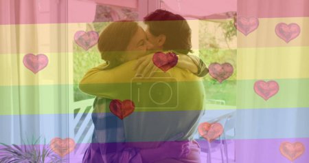 Foto de Imagen de emojis del corazón y la bandera del arco iris sobre la pareja femenina caucásica abrazando. Lgbtq, amor, romance y celebración concepto de imagen generada digitalmente. - Imagen libre de derechos
