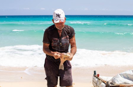 Téléchargez les photos : Un pêcheur étripe un poisson fraîchement pêché sur une plage cubaine 04 28 2022 - en image libre de droit