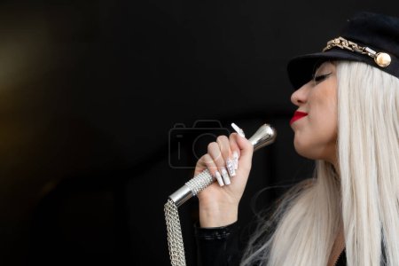 Latex outfit, hat for adult sex games. Young woman licks metal sex toy, blonde portrait