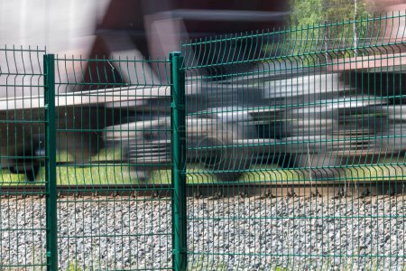 A metal fence behind which a train passes. Railroad fencing. Ensuring the safety of railway transport. Steel fence