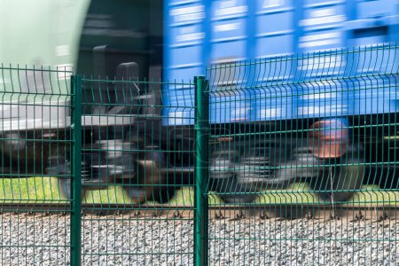 A metal fence behind which a train passes. Railroad fencing. Ensuring the safety of railway transport. Steel fence