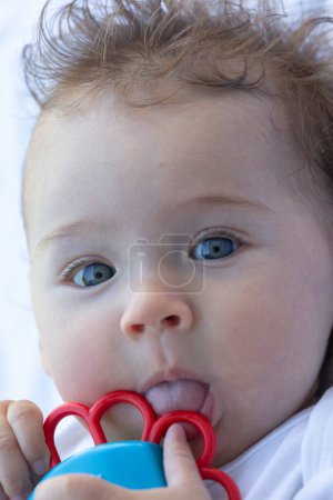Foto de Adorable bebé de cuatro meses sosteniendo un mordedor de juguete cerca del mes. Cara de bebé. Fondo blanco. - Imagen libre de derechos
