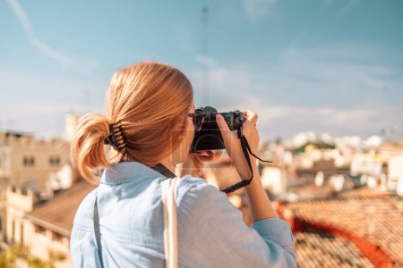 Téléchargez les photos : Touristes femmes positives photographiant prendre une photo de la maison avec appareil photo au coucher du soleil dans la vieille ville de Valence, Espagne. Vue arrière - en image libre de droit