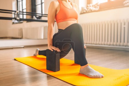 Schöne junge, fitte Frau beim Yoga-Workout mit Yoga-Blöcken auf Yogamatte im Yoga-Studio bei sonnigem Wetter