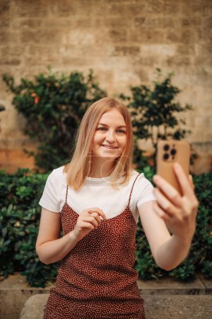 Téléchargez les photos : Charmante jeune femme dans une élégante robe de soie prend une photo selfie sur un téléphone portable dans le vieux quartier de Valence, Espagne. - en image libre de droit