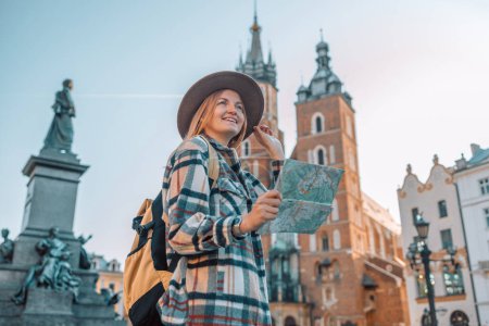 Téléchargez les photos : Vue réelle de voyageuse marchant sur la vieille place du marché à Cracovie tenant carte touristique. Concept de voyage et mode de vie actif. Photo de haute qualité - en image libre de droit