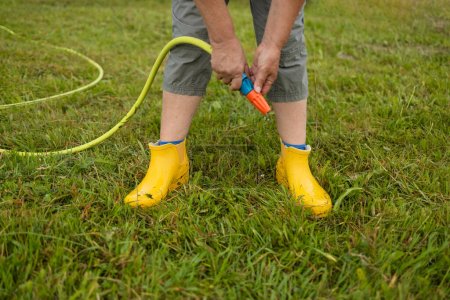 Photo for Washing of rubber boots. Close-up of a womans hands washes yellow rubber boots from mud with a garden hose in the garden after working in the ground - Royalty Free Image