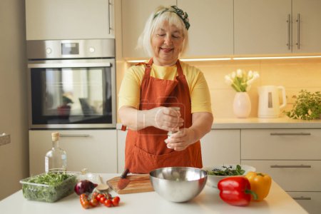 Foto de Primer plano de la mujer mayor está preparando ensalada de verduras en la cocina.Hembra agregando rúcula a la ensalada. Comida saludable. Ensalada Vegana. Dieta. Concepto de dieta. Un estilo de vida saludable. Cocinar en casa. Preparar alimentos - Imagen libre de derechos