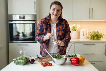 Foto de Retrato de una ama de casa está preparando deliciosa ensalada de verduras con tomate, rúcula, pimiento rojo y amarillo en la cocina. Comida saludable. Ensalada vegana. Dieta. Concepto de dieta. Estilo de vida saludable. Cocinar - Imagen libre de derechos