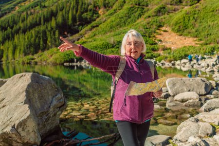Aufnahme einer Seniorin um die 60, die mit ihrem Smartphone eine Landkarte hält, während sie die Aussicht von der Spitze eines Berges genießt. Touristinnen sitzen auf einem Felsen in den Bergen und lesen die Landkarte. Polen, Tatry 