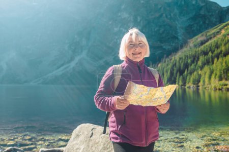 Prise de vue d'une femme âgée des années 60 perdue avec un téléphone intelligent tenant une carte tout en admirant la vue depuis le sommet d'une montagne. Touriste féminine est assis sur le rocher en montagne lire la carte. Pologne, Tatry 