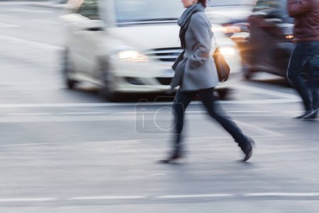 Téléchargez les photos : Picture with motion blur of a woman who crosses a street in the city, with waiting cars in the background - en image libre de droit