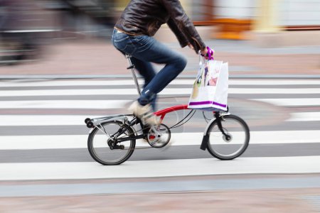 Téléchargez les photos : Image avec flou de mouvement intentionnel d'un homme avec un sac à provisions monte un vélo pliant - en image libre de droit