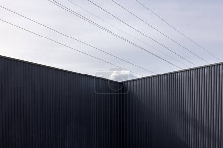 Foto de Esquina de un edificio industrial de hierro corrugado y líneas eléctricas contra el cielo - Imagen libre de derechos