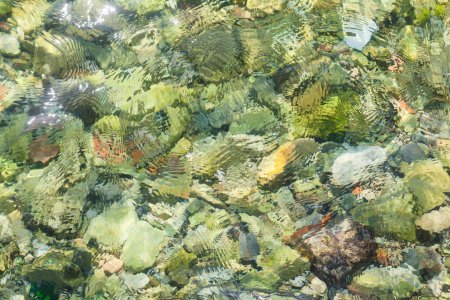 Téléchargez les photos : Texture de fond de la surface de l'eau ondulée avec des pierres de galets sur le sol - en image libre de droit