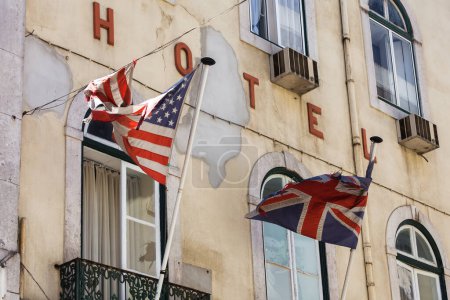 Téléchargez les photos : Vieille façade d'hôtel délabrée avec des drapeaux déchirés des États-Unis et du Royaume-Uni devant - en image libre de droit