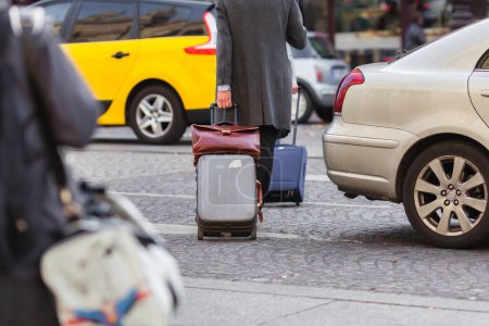 Téléchargez les photos : Image d'une scène de rue d'un inconnu tirant une valise à roues derrière lui et traversant une rue - en image libre de droit